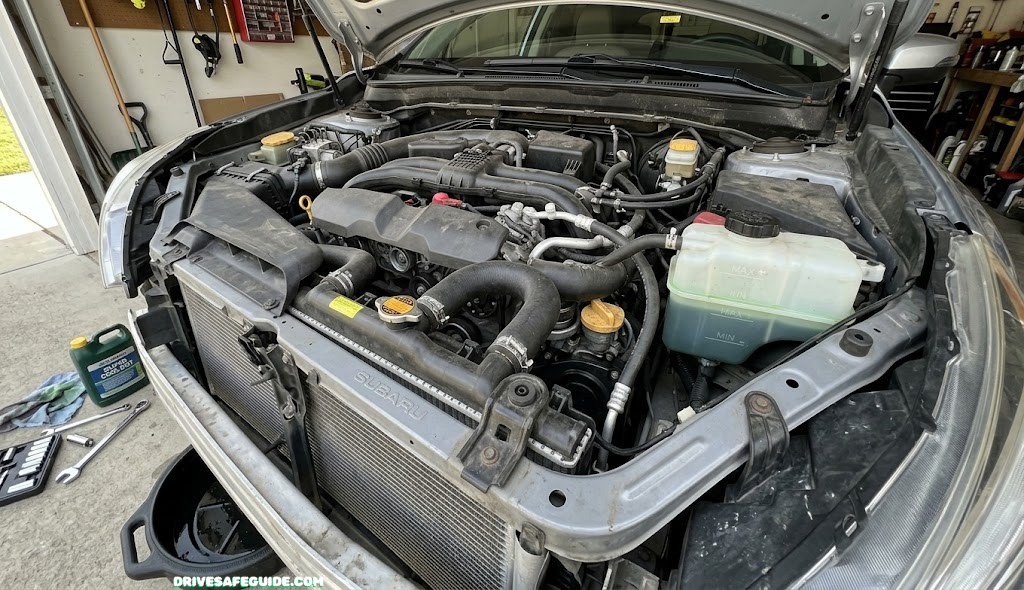 Overview of a car's radiator, hoses, and coolant reservoir in the engine bay before a DIY flush